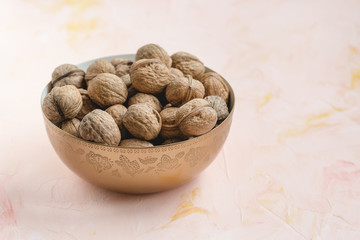 Uncracked walnuts in shell in bowl on pink background, concept of healthy eating vegan food. Close up, selective focus, copy space.