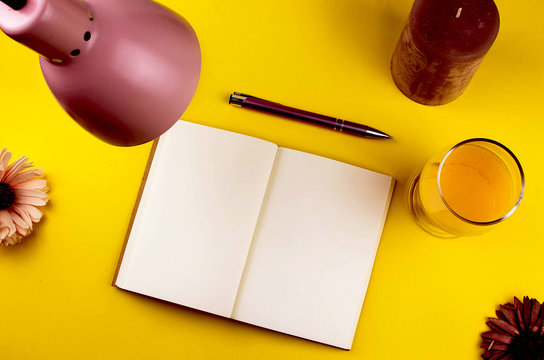 Workspace empty, cleean notepad with copy space and lamp and flowar and orange juice on the yellow background 