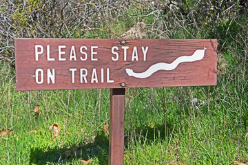 A sign warns hikers to stay on the trail due to the prevalence of rattlesnakes in the undergrowth in Arizona.