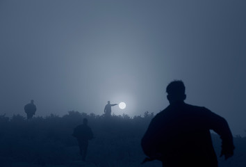 Fototapeta premium silhouette of men running towards setting sun, artistic image