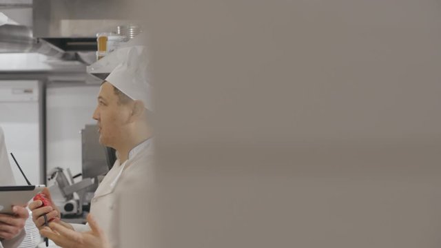 Two cooks with digital tablet over restaurant kitchen background