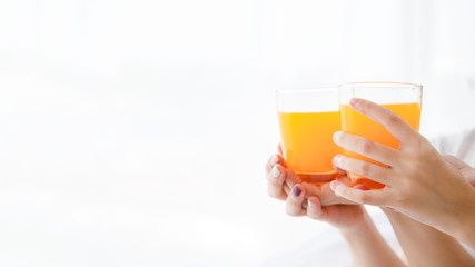 Close up women's hand hold glass of orange juice on bright background with copy space on left side.