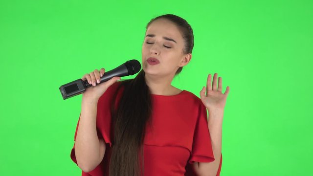 Portrait of pretty young woman is singing into a microphone and moving to the beat of music. Green screen