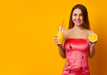 Obraz premium Portrait of a happy smiling woman holding a glass of fruit juice, half an orange on a yellow background