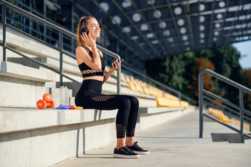 Fototapeta na wymiar Attractive young healthy sportswoman listens to music with earphones during training at the stadium.