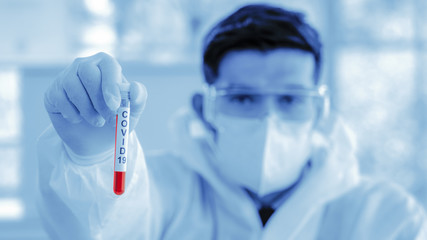 coronavirus covid-19 infected blood sample in sample tube on hand of scientist in biohazard...