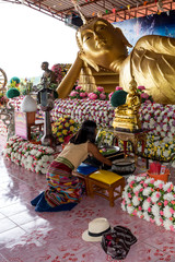 Woman praying in wat to reclining Buddha  surrounded by flowers