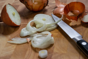 Close up of onion rings on a wooden cutting board, with a small kitchen knife.