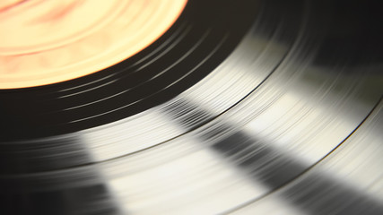 An abstract view of the rotating motion of a black vinyl disc. Daytime natural light reflections on the soundtrack surface. Top view scene.