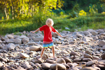 Child hiking in mountains. Kids at river shore.
