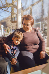 Fototapeta premium Small caucasian boy grandson child sleeping by his grandmother embracing while sitting at home or at the restaurant cafe in sunny day nursery