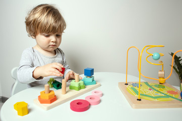 Beautiful toddler play with a wooden toys at home. Toddler play with a color educational toy.  Child play at the table in the baby room. Child development.  Funny baby. Lifestyle.