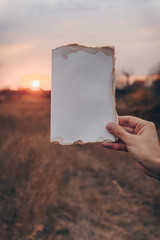 Blank greeting card. Vintage old rustic background. Wedding invitation card paper on sunshine background. Hand holding empty card in a park in sunny rays. Copy space.Mockup.