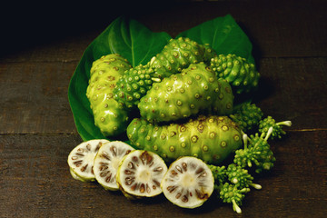 Pile of Noni fruit or Morinda Citrifolia and green leaf on wooden background, dark tone. Fresh noni are high nutrients and antioxidants.