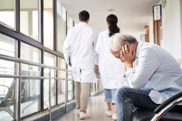 devastated senior asian man sitting in hospital hallway