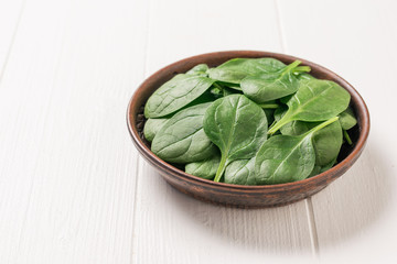 Fresh spinach leaves in a clay bowl on a white rustic table. Food for fitness. The view from the top.