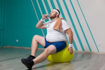 Overweight man is sitting on a fitness ball exhausted after a hard training in group fitness...