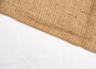 Brown burlap laying on white sheet, close up view. Abstract background. Texture of sackcloth. Background for banners, or wallpapers