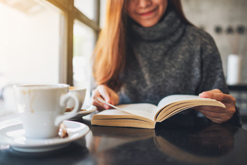 Closeup image of a beautiful woman holding and reading a book with coffee cup on the table
