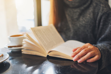Closeup image of a beautiful woman holding and reading a book with coffee cup on the table
