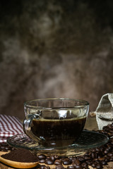 Black coffee in a clear glass on a wooden table with roasted coffee beans and a spoon