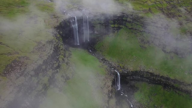 Tall Foss&aacute; Waterfall on Faroe Islands coastline, high aerial pan above clouds