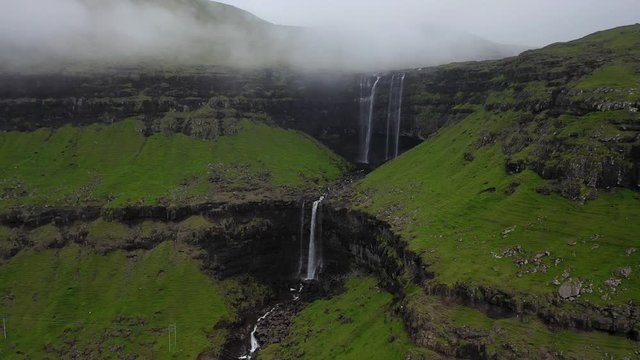 Foss&aacute; Waterfall with power line over river in cloudy Faroe Islands, aerial pull away