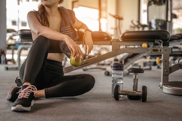 Woman sitting holding an apple after a workout in the gym at sunset. fitness ,workout, gym exercise ,lifestyle  and healthy concept.