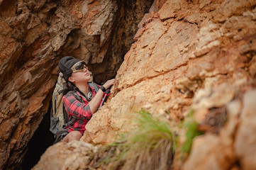 Fototapeta premium Side view of woman hiker climbing on the cliff at cave in sunset. Woman, hiking, hikers, mountain, cave, activity concept.