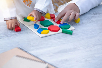 Close up hand of little Muslim boy with tradition suit and mom playing colorful wood blocks in the park, education concept