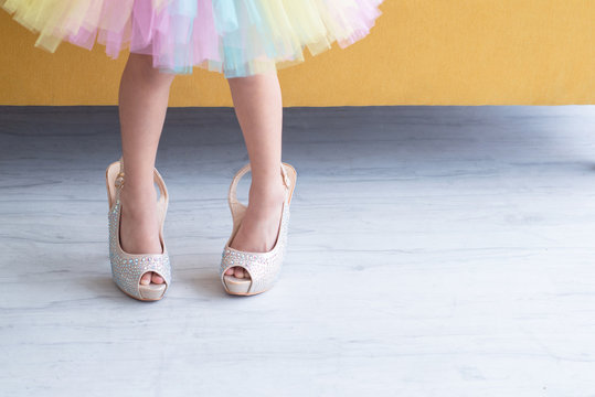 Little fashionista girl in elegance shoes on high heels with rainbow dress