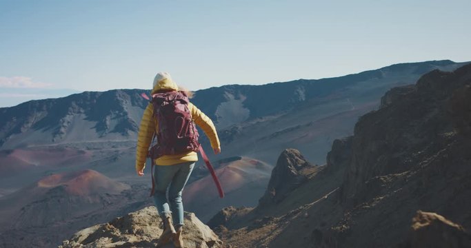 Young adventurous woman walking to the edge of a cliff and raising her arms in joy, backpacker enjoying a mountain view, amazing trekking adventures outdoors