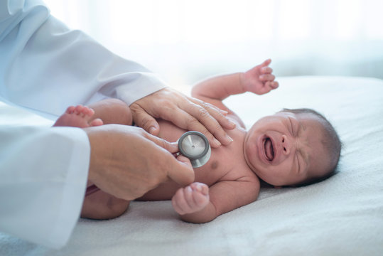 Doctor with stethoscope listening to heartbeat of newborn baby