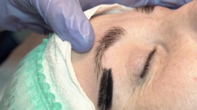 In the eyebrow beauty salon, the master takes care of the eyebrows. Design and coloring styling and lamination of female eyebrows. Color matching. Correction with a cosmetic tool.