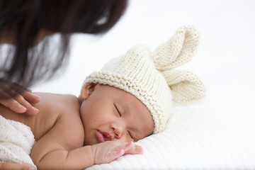 A 1-month-old infant is wearing a wool hatt is sleeping on the white futon. The rest of the newborn baby.