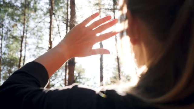 Closeup 4k video of young woman looking on bright sun through her fingers in the forest