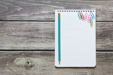 Notepad with a blank white sheet in a checker paper with simple graphite pencil and with paper clips lies on the background of wooden boards.