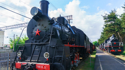 View of old classic black steam locomotives with red decoration on railroad track on sky background.