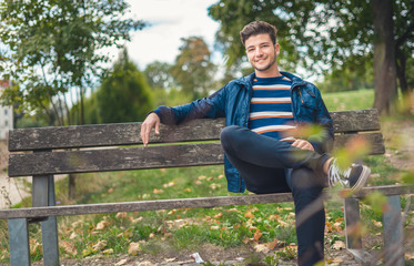 Positive young man with smile on his face sitting on bench