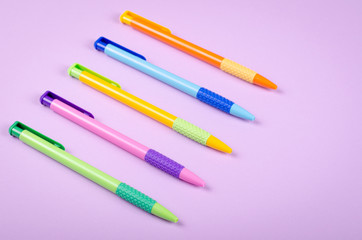 Different colored pens, school ballpoint on purple background composition.