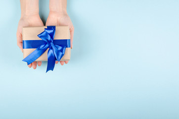 Hands with gift box on blue background composition, present with ribbon and bow.