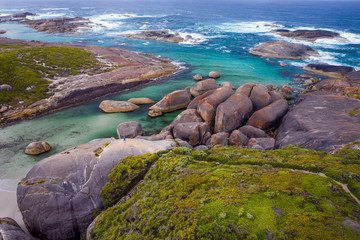 Man standing on top of Elephant Rocks, looking at view of huge orange and ocre oval shaped, granite rocks in green pools by the beach on the South Coast of WA.