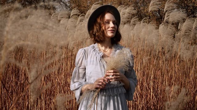 Pregnant Young Woman Holding A Fluffy Grass In The Autumn Field
