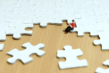 Business strategy conceptual photo - Miniature young men siting on jigsaw puzzle piece while reading
