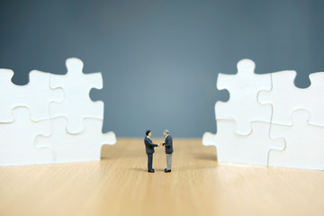 Business strategy conceptual photo - Miniature businessman make handshake partnership in the center of jigsaw puzzle piece that are arranged - Powered by Adobe