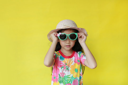 Young child girl in summer dress and hat wearing a sun glasses over yellow background with copy space