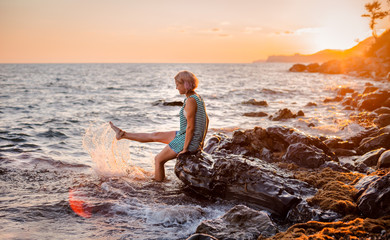 One young beautiful girl splashes and splashes the sea at sunset. Summer landscape sea, Islands and orange sunlight.