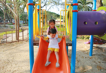 Happy asian sister and her little brother enjoy playing slider in playground in the park. Child...
