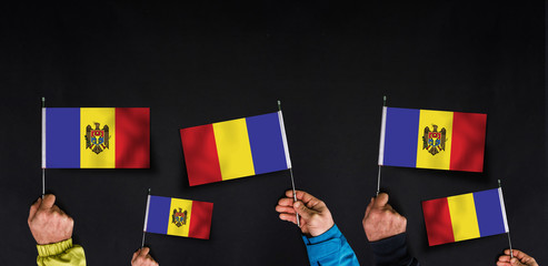 Fototapeta na wymiar Hands holds flags of Moldova on dark background