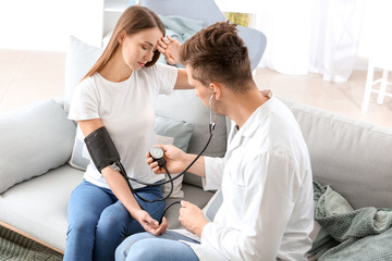 Doctor measuring blood pressure of young woman at home